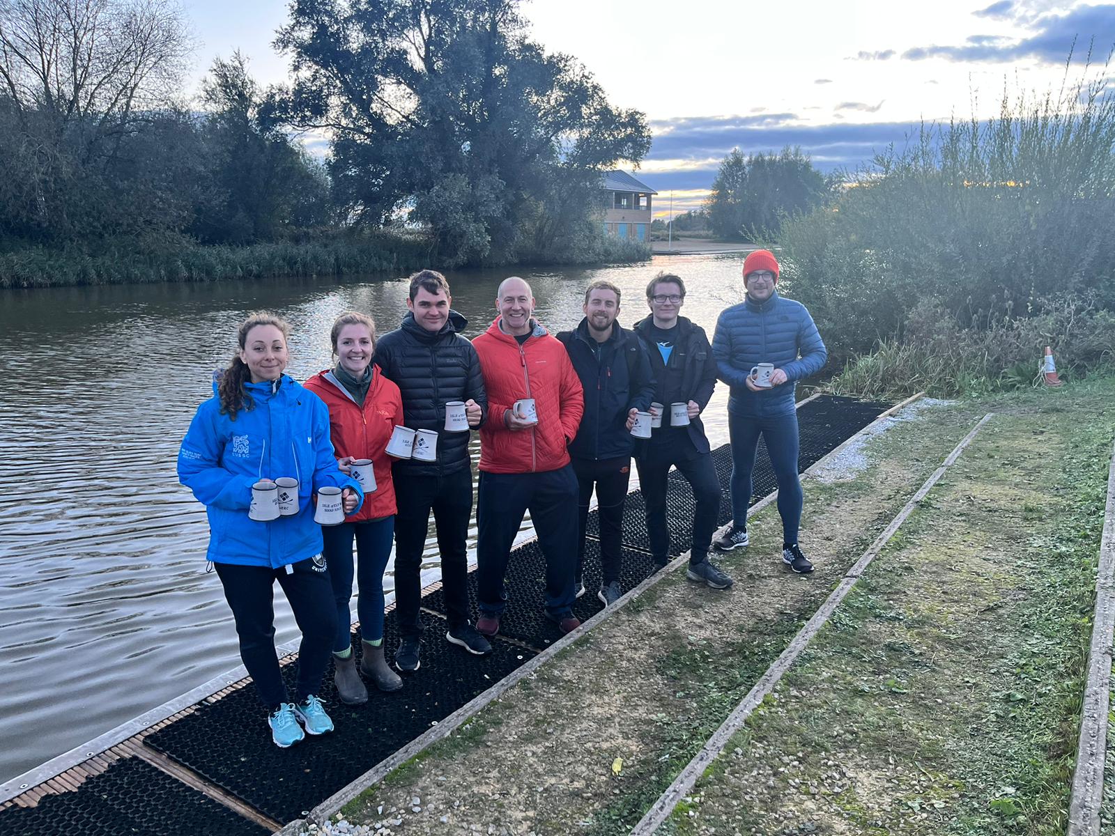 St Neots Rowing Club rowers stand in front of the river at Ely holding their winners pots
